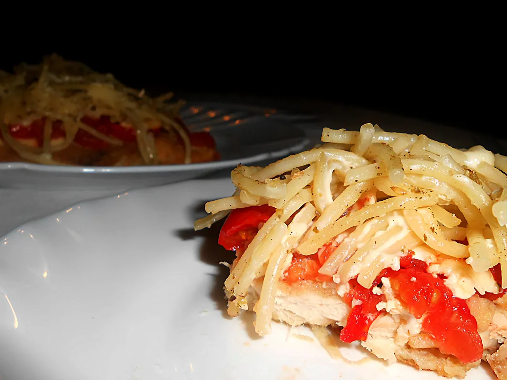 Pohovani fileti prekriveni sirom, paradajzom i špagetima